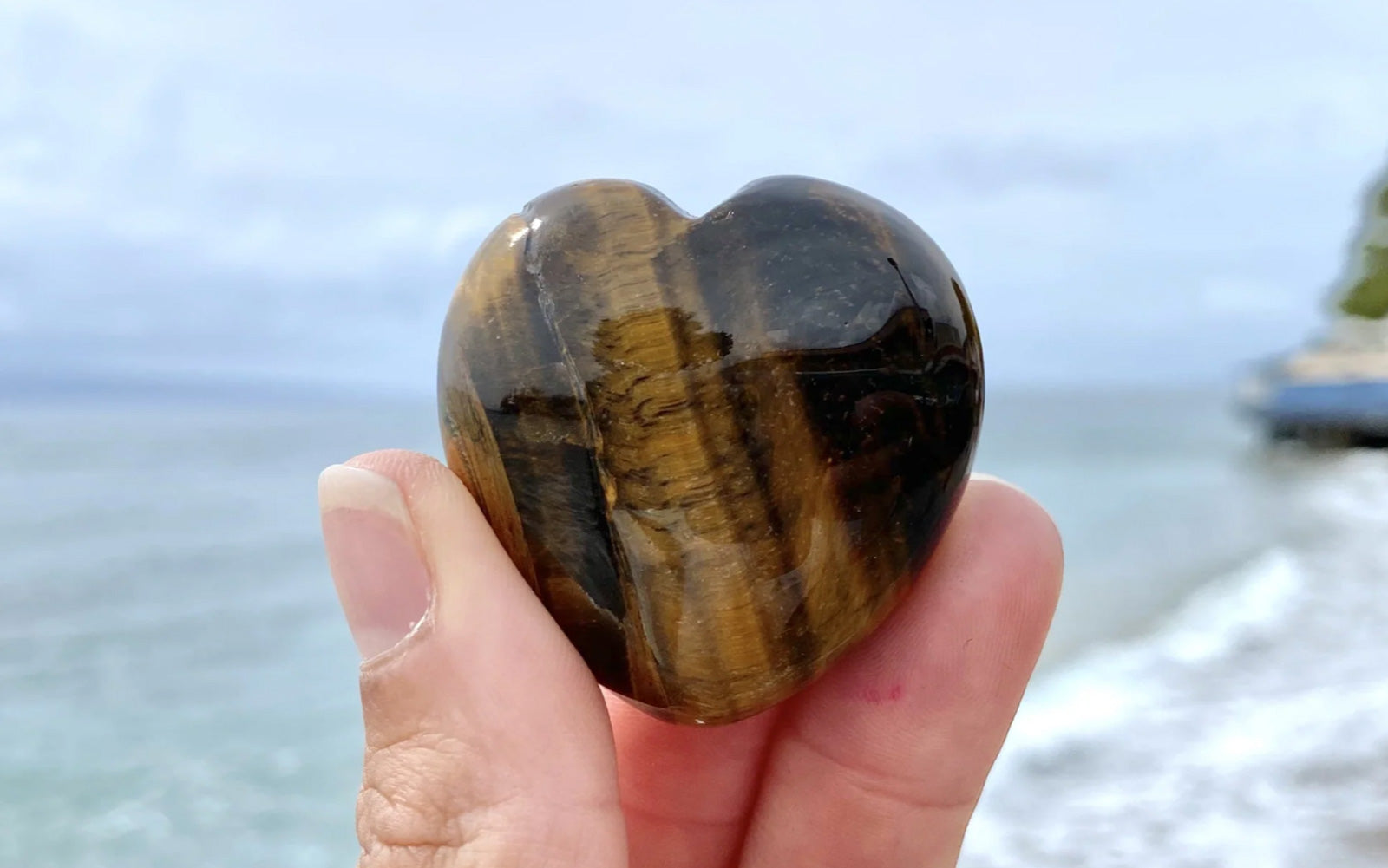 Hand holding up healing crystal tiger eye stone in shape of a heart