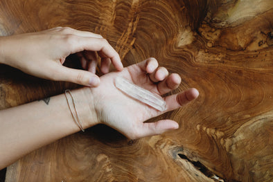 Woman's hands holding a quartz crystal over a wood surface