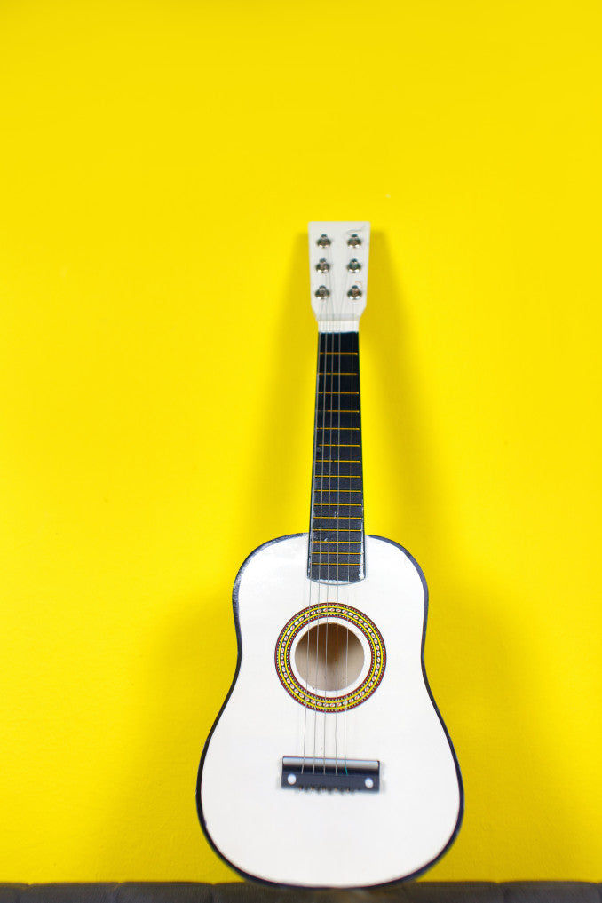 white ukelele leaning against yellow wall